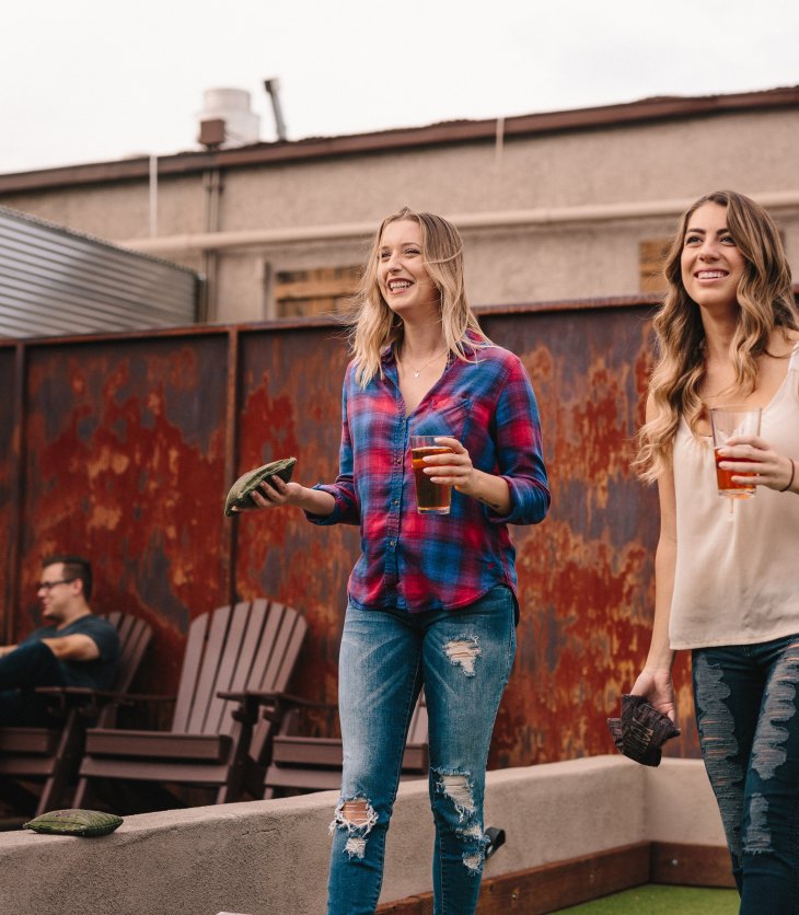 Two young women playing cornhole on rooftop