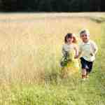 little girl holding a basket of flowers and holding hands with a little boy in a grassy field |lawnmower parenting